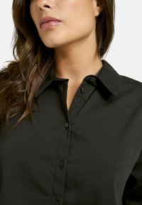 Black button-up shirt featuring a structured collar, smooth texture, and a slim fit. Buttons are dark and positioned along the front placket.