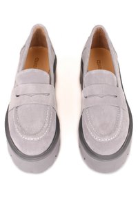 Een paar lichtgrijze suede instappers met dikke zwarte zolen en zichtbare witte stiksels op een witte achtergrond.