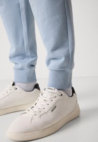 Hvite lær sneakers med svarte detaljer, teksturert snøring, gummisåle. Kombinert med lyseblå joggebukser med ribbekant.