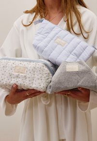 Tre kosmetikkvesker: en hvit med små blomstertrykk, en lys blå med striper, og en grå, alle med glidelåslukking og stoffmerking.