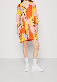 Wielokolorowa sukienka z abstrakcyjnymi wzorami w odcieniach pomarańczowego, różowego, żółtego i fioletowego, z dekoltem w serek, zapięciem na guziki z przodu oraz bocznymi kieszeniami.