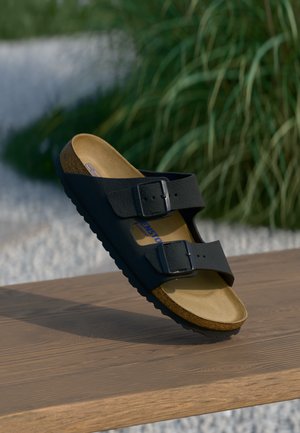 Sort sandal med to justerbare spænder, kork- og skumfodbed, teksturerede syntetiske remme og en holdbar gummisål.