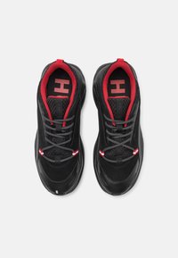 Chaussures de sport noires avec des accents rouges, des panneaux en mesh texturé et des lacets gris. La doublure intérieure est rouge avec un logo "H" bien visible.