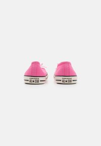 Zapatillas de lona de caña baja en color rosa con suelas de goma negra y acentos blancos. Incluyen un diseño con cordones y la marca "CONVERSE ALL STAR" en el talón.