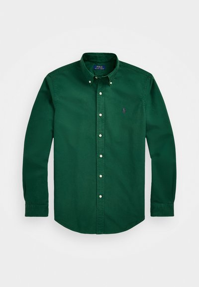 Zelena bombažna srajca z dolgimi rokavi in gumbom navzdol, z navadnim ovratnikom, belimi gumbi in majhnim vijoličnim logotipom na prsih.