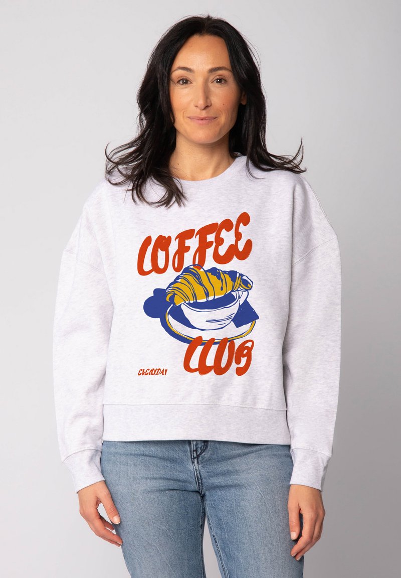 Hellgraues Sweatshirt mit einem grafischen Druck eines Croissants und einer Kaffeetasse, versehen mit rotem und blauem Text, der "COFFEE CLUB" liest.