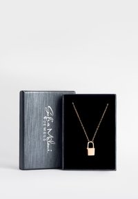 Guld hänglåspendel på en delikat kedja, uppvisad i en texturerad svart smyckesbox med logotyp i silvertryck. Sammetinre.