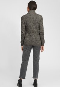 Grijze gebreide trui met hoge kraag, gestructureerd patroon en aansluitend ontwerp, gecombineerd met grijze jeans en zwarte enkellaarsjes.