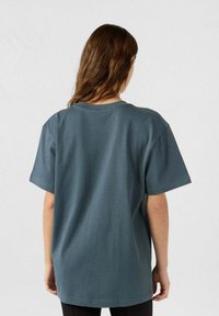 T-shirt di cotone blu ardesia con vestibilità comoda, maniche corte e scollatura rotonda. Il tessuto ha una texture liscia e un design semplice.