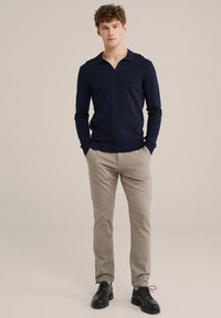 Pulover tricotat de culoare albastră închisă cu guler, asociat cu pantaloni slim-fit bej și pantofi negri cu șireturi, pe un fundal neutru.