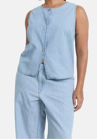 Vaaleansininen farkkaliivi, jossa pyöreä pääntie ja etupainonappi. Suora leikkaus, jossa on minimaalisesti saumoja.