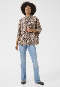 Camicia a stampa leopardata in tessuto leggero, design con bottoni, colletto, maniche a tre quarti, abbinata a jeans svasati azzurri chiari e ballerine nere.