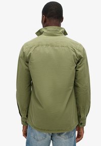 Jasnozielona, długosleeve koszula z kołnierzem stojącym, mankietami zapinanymi na guziki i teksturowanym wykończeniem. Posiada szwy yoke na plecach oraz luźny krój.