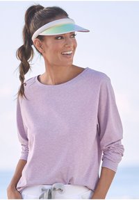 Hellblau-langes Oberteil mit lockerer Passform, ausgestattet mit Raglanärmel. Kombiniert mit einer weißen Schirmmütze, die einen reflektierenden, irisierenden Schirm hat.