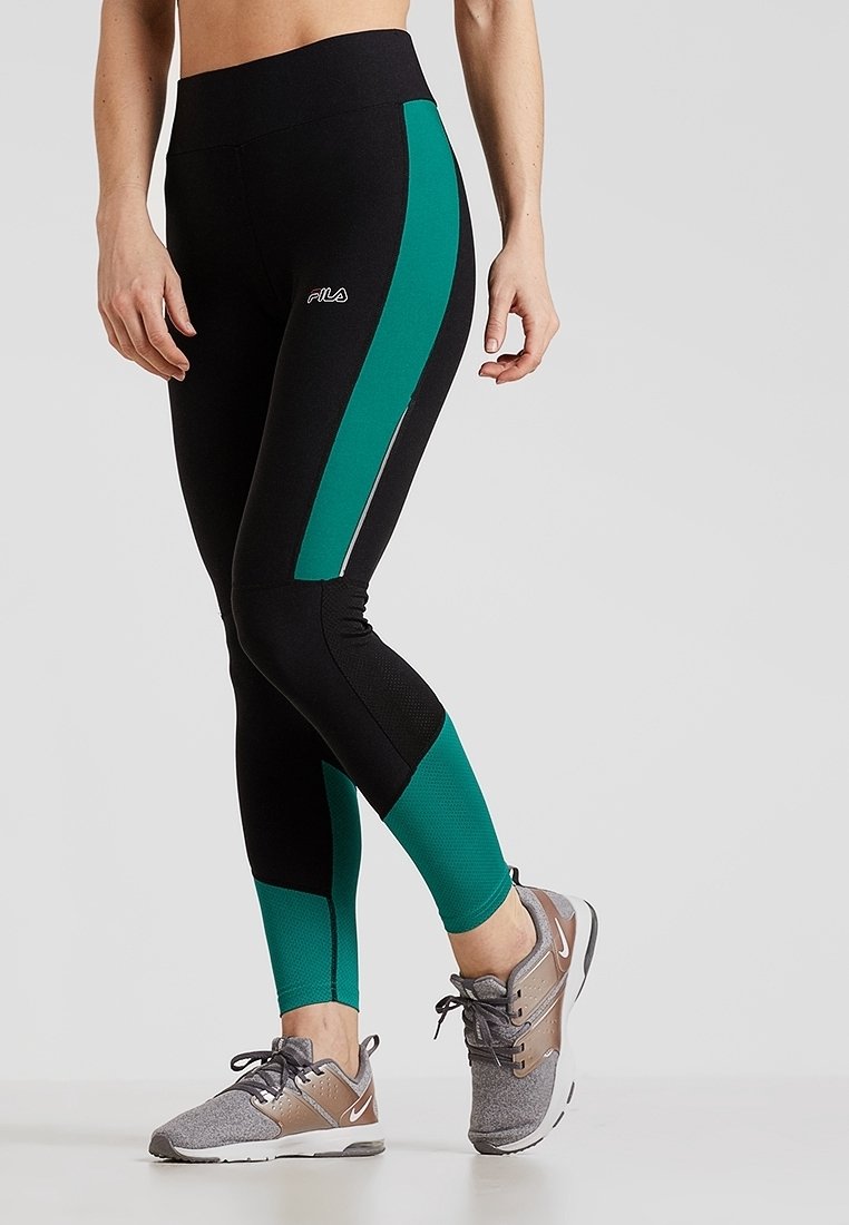 Czarne legginsy z turkusowymi bocznymi panelami, z wysokim stanem i siateczkową teksturą w dolnej części. Połączone z szarymi sportowymi butami.