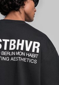 Black oversized t-shirt with white text, featuring the words "STBHVR BERLIN MON HABIT CREATING AESTHETICS" prominently displayed on the back.