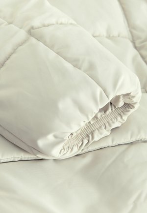 Cuvertură de pat de culoare deschisă, matlasată, cu o textură netedă și moale. Are o margine pliată și umplutură pufoasă pentru izolație.