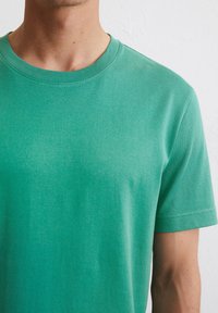T-shirt vert à manches courtes en tissu lisse. Présente un col rond et une coupe ajustée. La texture semble douce et respirante.