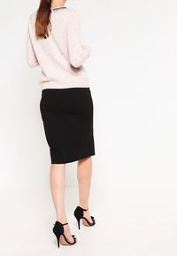 Ljusrosa tröja med en texturerad yta, kombinerad med en figursydd svart pennkjol och svarta högklackade sandaler. Anmärkningsvärd detalj på ryggen av tröjan.