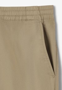 Beige vevde bukser med elastisk midje og sidelommer. Har en myk tekstur og en subtil diagonal mønster.