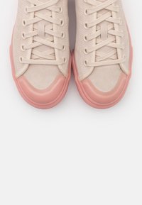 Beiga mockasinsneakers med rosa gummisulor, med snörning och rundade tår. Slät textur med subtila sömdetaljer.