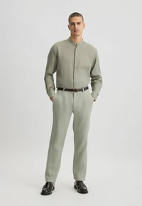 Hellgrünes Hemd mit Stehkragen, kombiniert mit passenden hellgrünen Hosen. Das Outfit zeichnet sich durch eine glatte Textur und minimale Akzente aus.