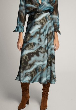 Jupe midi à motifs bleus et noirs portée avec un chemisier assorti et des bottes marron en daim jusqu’aux genoux.