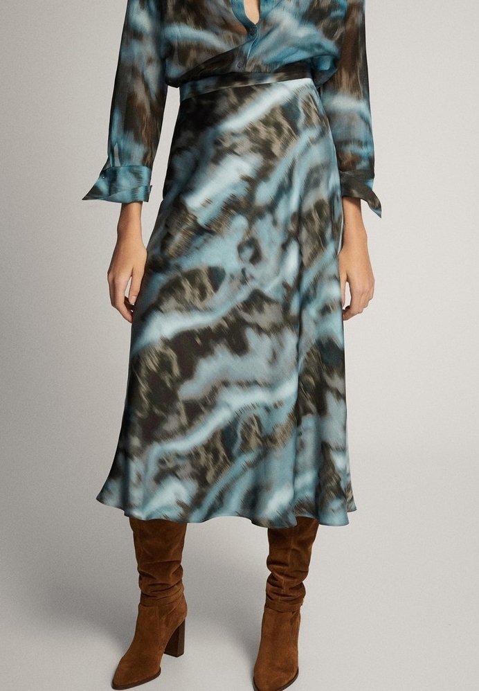 Jupe midi à motifs bleus et noirs portée avec un chemisier assorti et des bottes marron en daim jusqu’aux genoux.