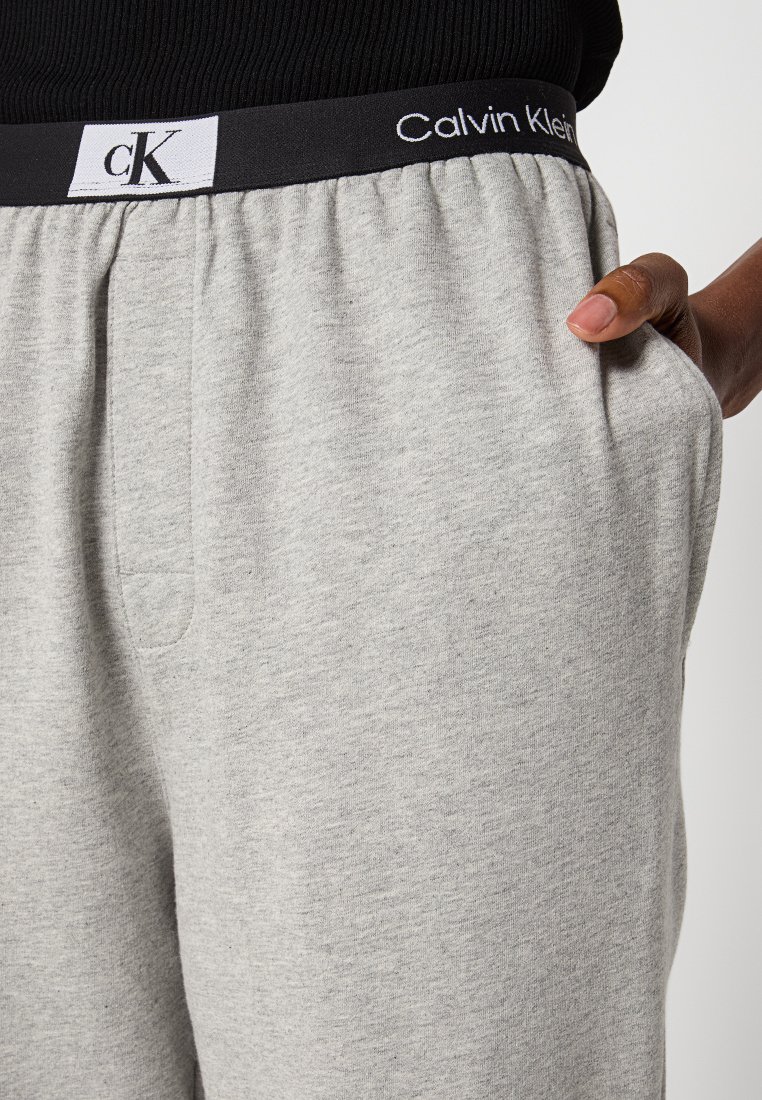 Pantaloni della tuta grigi con una vita elastica nera che presenta il logo Calvin Klein. Hanno tasche laterali e un tessuto morbido e texturizzato.