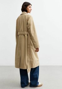 Beige trenchcoat met een ceintuur in de taille, lange mouwen en een relaxte silhouet; heeft een klassieke kraag en een enkel-lange ontwerp.