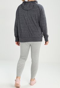 Tmavě šedá mikina s kapucí z jemného materiálu, doplněná světle šedými legínami se bílým logem Nike a bledě růžovými sportovními botami.