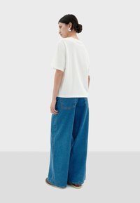 Witte top met korte mouwen, gecombineerd met losse, hooggetailleerde blauwe denim broek. De stof lijkt zacht, met een comfortabele pasvorm en minimale details.