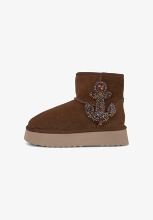 Brown suede ankle boot with a thick, light-colored platform sole, featuring a jeweled anchor design on the outer side.