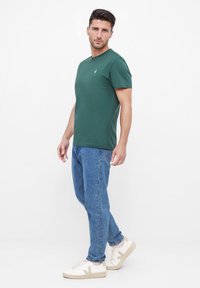 Groene t-shirt met korte mouwen en een ronde hals, gecombineerd met lichtblauwe jeans en witte sneakers met beige accenten.