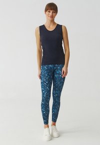 Marineblauw mouwloos topje gecombineerd met blauwe leggings met een gemustreerd ontwerp, aangevuld met witte sneakers.