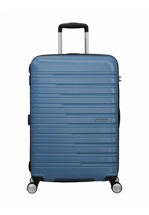 Valigia rigida di colore blu con design a coste testurizzato, manico retrattile e quattro ruote girevoli per una facile mobilità. Logo del marchio visibile.
