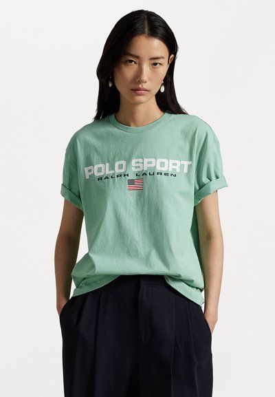 Minta zaļa kokvilnas T-krekls ar sarullētām piedurknēm, ar uzrakstiem "POLO SPORT" un "RALPH LAUREN" baltā krāsā un mazu Amerikas karoga dizainu.