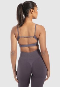 Paarse sport-bh met verstelbare schouderbanden en een crossover-achterkant. Gedragen met bijpassende high-waisted leggings, die een glad ribbeltextuur tonen.