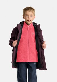 Veste pour jeunes avec une couche extérieure violette et une doublure intérieure en polaire rose vif, dotée d'une fermeture éclair complète et d'accents noirs. Portée avec un pantalon bleu marine.