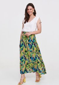 Maxi spódnica w intensywny zielony tropikalny wzór, zestawiona z białą bluzką z dekoltem w serek. Żółte, blokowe obcasy dopełniają całość.