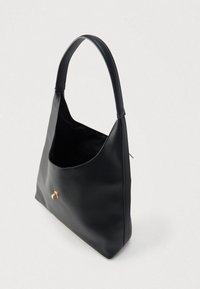 Svart skulderveske i skinn med teksturert overflate, buet form, ett håndtak og en liten gyllen dekorasjon på forsiden. Interiøret er synlig.