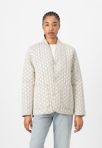 Chaqueta acolchada con un patrón geométrico en tonos crema y beige, con un cuello tipo chal y dos bolsillos frontales. Textura suave y corte relajado.