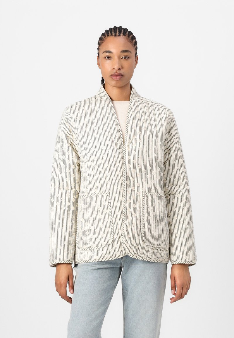 Chaqueta acolchada con un patrón geométrico en tonos crema y beige, con un cuello tipo chal y dos bolsillos frontales. Textura suave y corte relajado.