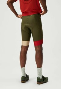 Olijfgroene fietsshorts met een lichtbeige en rode band aan de zoom. Het materiaal is rekbaar met een gevoerd zitgedeelte, ontworpen voor prestaties.