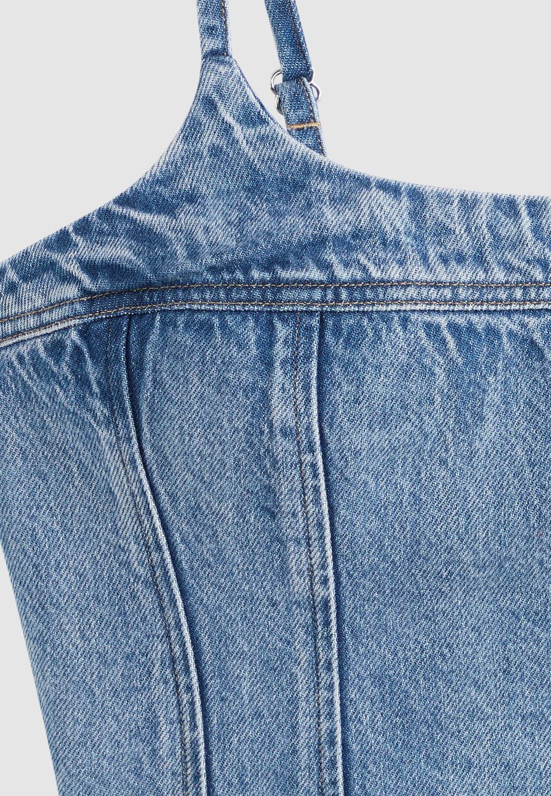Top blu denim con spalline sottili, cuciture visibili e dettagli di cucitura, che mostra la parte superiore della schiena su uno sfondo chiaro.