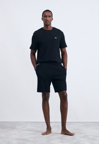 T-shirt preta de manga curta e calções combinando, feitos de um tecido leve. Apresenta um logótipo discreto no peito e bolsos nas costuras laterais.