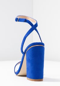 Sinisen mokkanahkaisen korkean korkokenkän paksu blokiorko, nilkkaremmillä ja avoimella varpaalla. Sisältää sileän sisävuoren ja erottuvan pohjan.