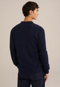 Mörkblå tröja med ribbat mönster, rund halsringning och åtsittande ärmar. Designad med en klassisk passform och minimal detalj på baksidan.