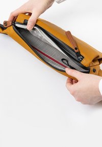 Gelbe Lederhandtasche mit einem Reißverschluss, ausgestattet mit einem gefütterten Innenraum mit einem Rautenmuster und einer roten Akzenttasche.