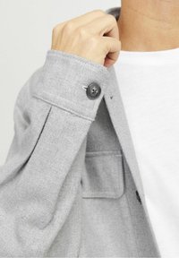 Šedá košile z vlněné směsi s dlouhými rukávy, zapínáním na jeden knoflík a prošitými detaily. Obsahuje náprsní kapsu a texturovanou látku.